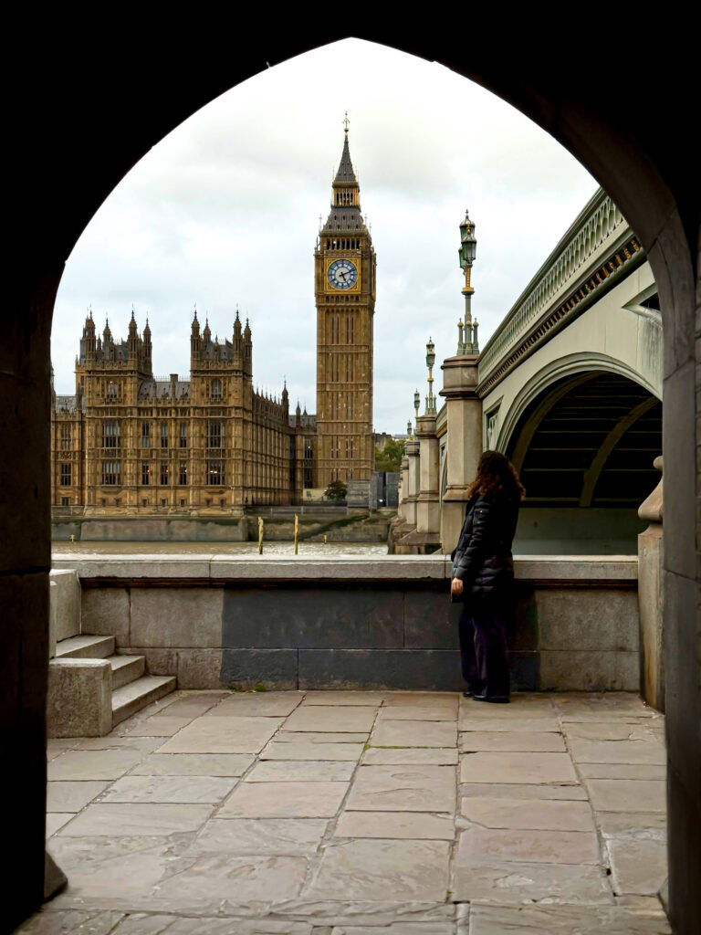 Big Ben enmarcado por un arco bajo el puente de Westminster, con una persona observando la torre.